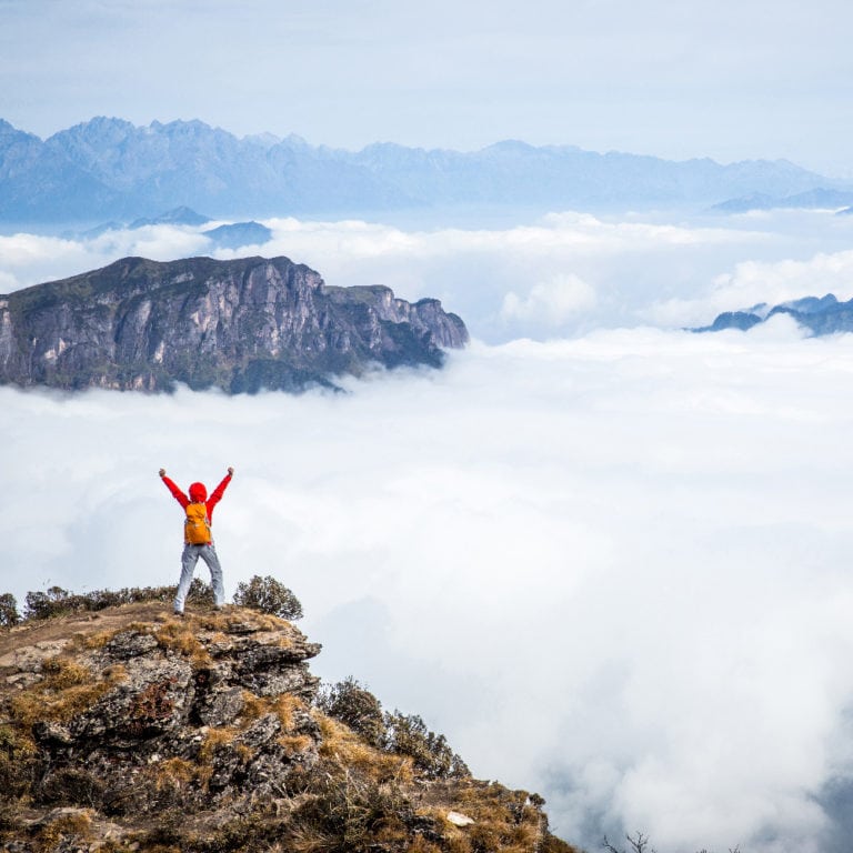 Person at the top of the mountain raising their hands in freedom