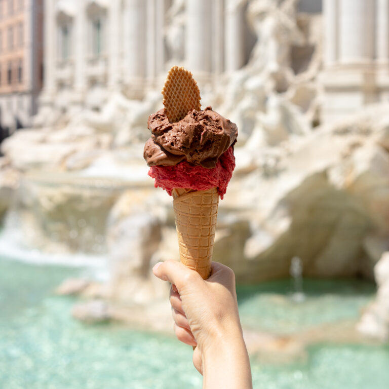 Hand holding a gelato in front of the Trevi fountain.