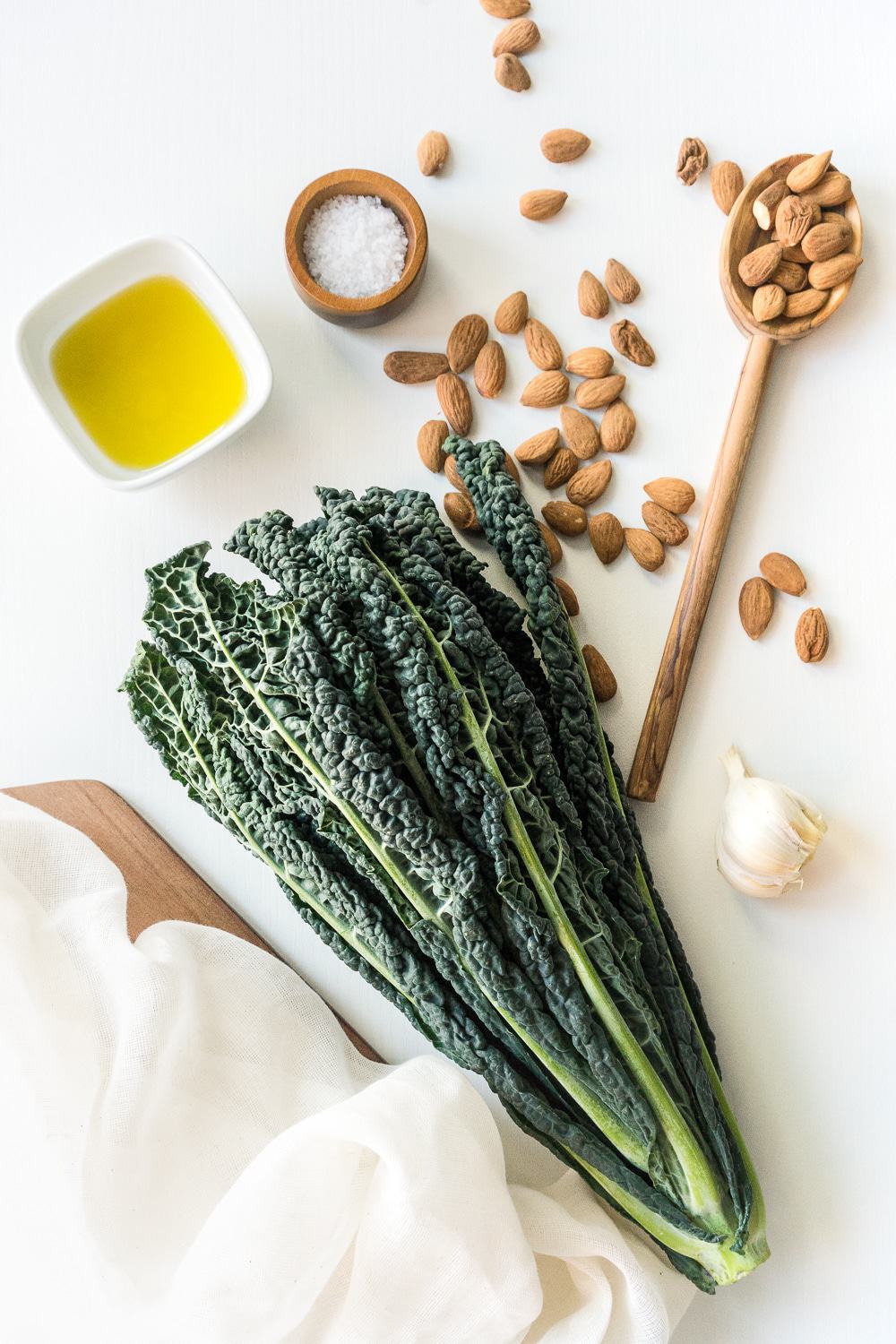 Top view of all ingredients: Tuscan kale (also known as black kale or lacinato kale), almonds, garlic, salt, and extra-virgin olive oil.
