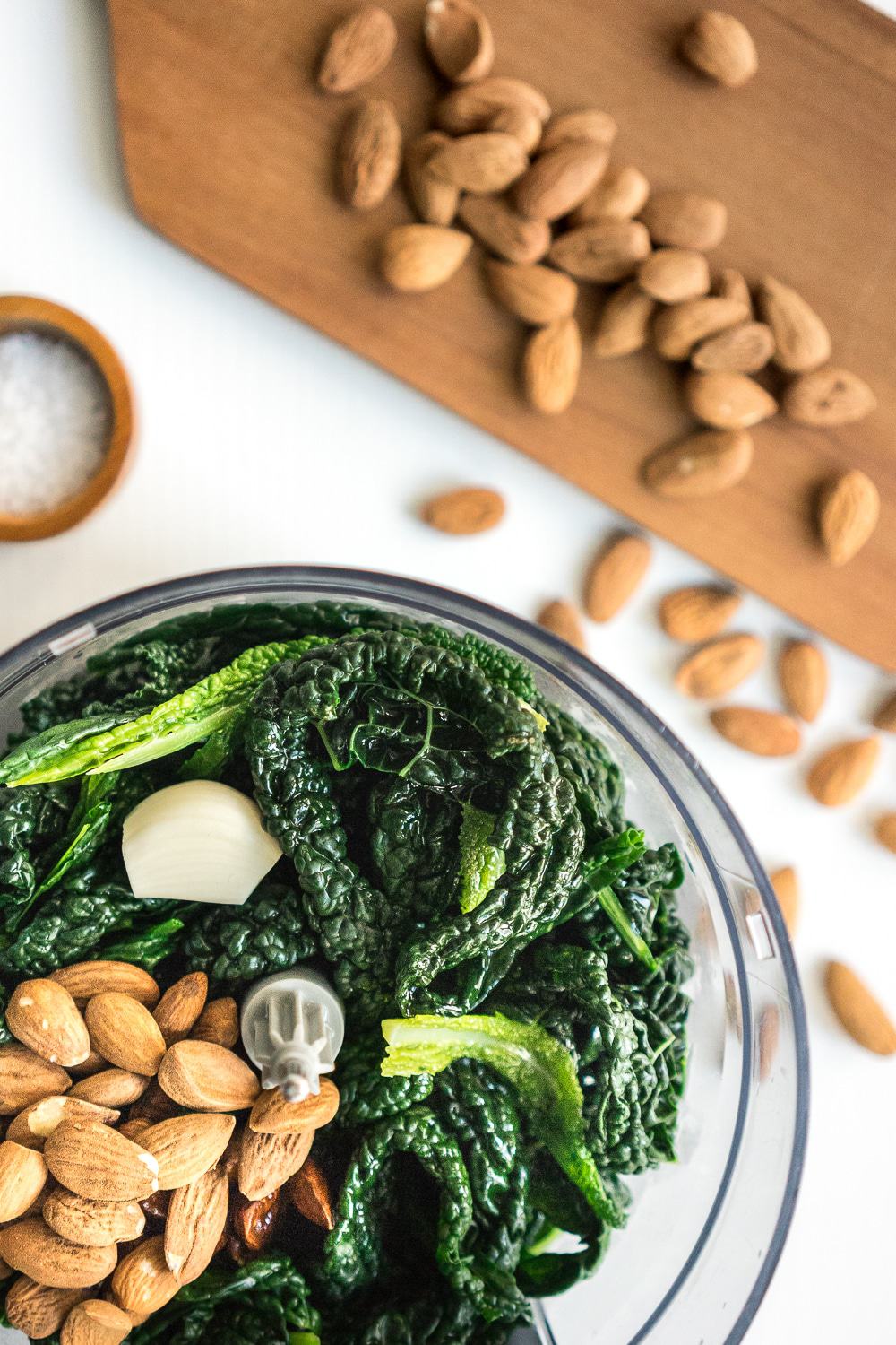 Top view of food processor with black kale (Tuscan kale) leaves and almonds.