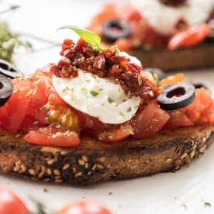 This perfect grilled bruschetta with mozzarella and tomatoes recipe will make your summer BBQ special! Grilled smoky bread, delicious sun-ripened tomatoes, sun-dried tomatoes, extra virgin olive oil, delicious mozzarella and black olives make this the ultimate appetizer for your summer parties!