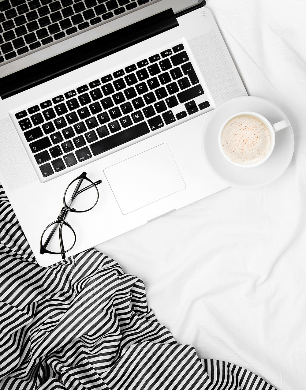 Top view of a laptop and coffee on a bed