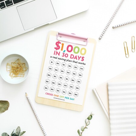 Top view of desk with a laptop and a printable of a $1000 monthly challenge