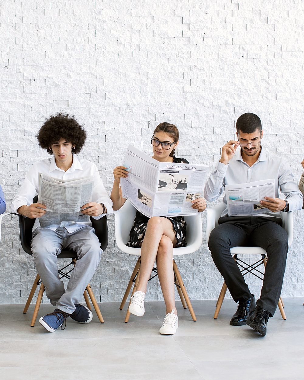 People reading business newspapers, waiting to be called to a focus group. 