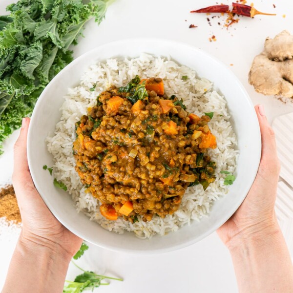 Top view of hands holding a white plate with coconut lentil curry and basmati rice.