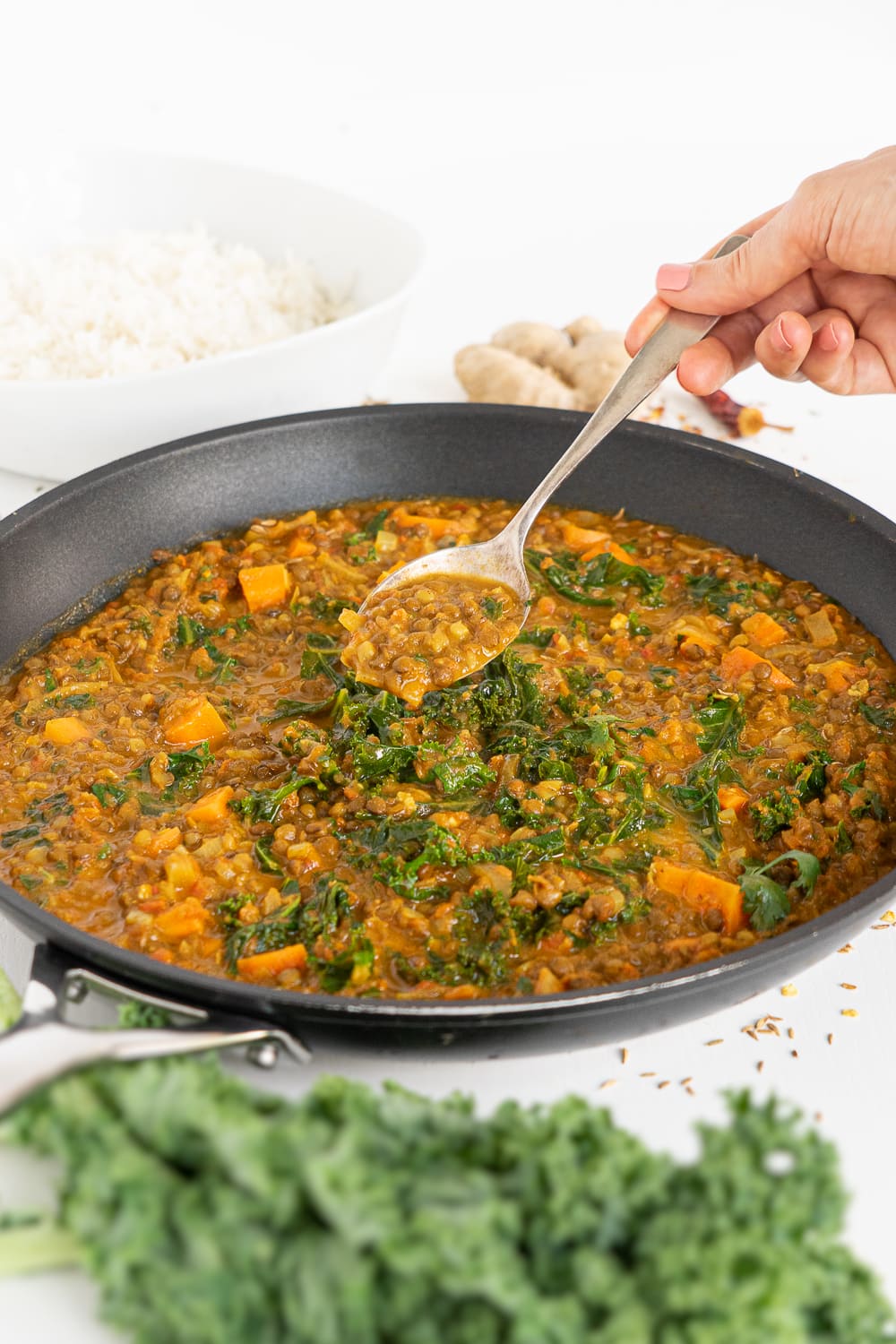 Large pan with cooked coconut lentil curry with hands holding a spoon to show the curry.