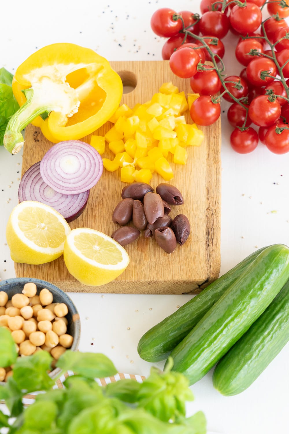 Top view of ingredients to prepare a Mediterranean quinoa salad: Yellow bell pepper, cherry tomatoes, kalamata olives, lemon, red onions, chickpeas and basil