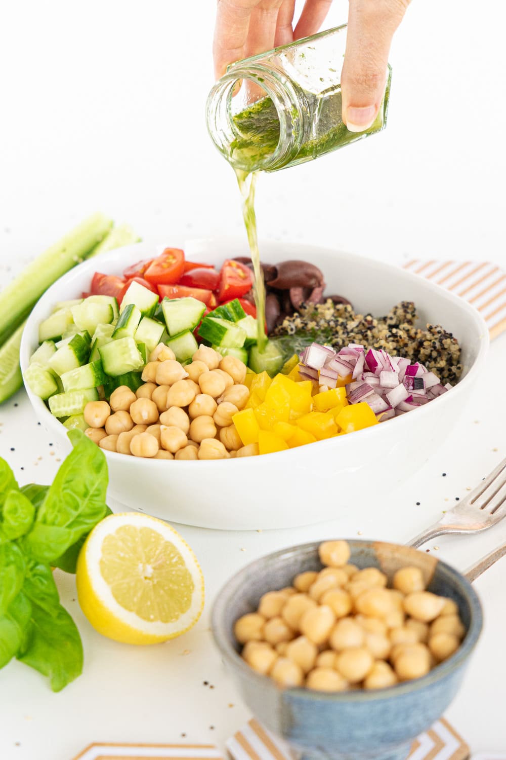 Three quarter view of Mediterranean Quinoa salad in a white bowl while hand is versing mediterranean dressing on it