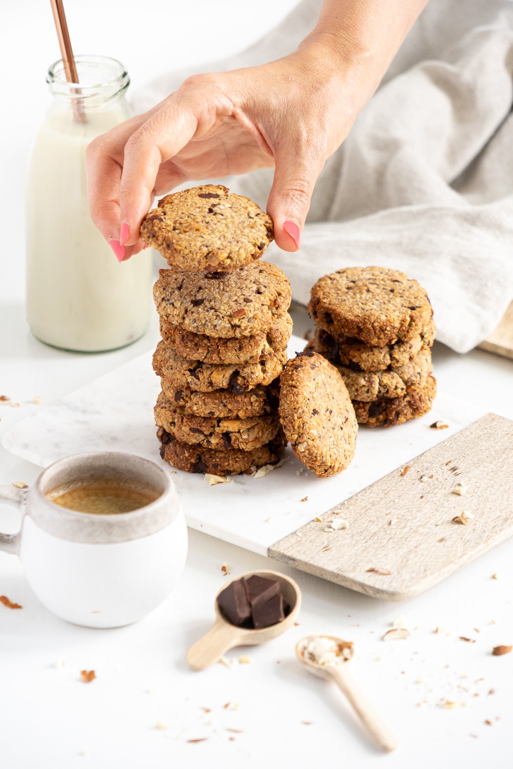 A pile of breakfast cookies with coffe and milk with one hand adding the last cookie on top of the pile