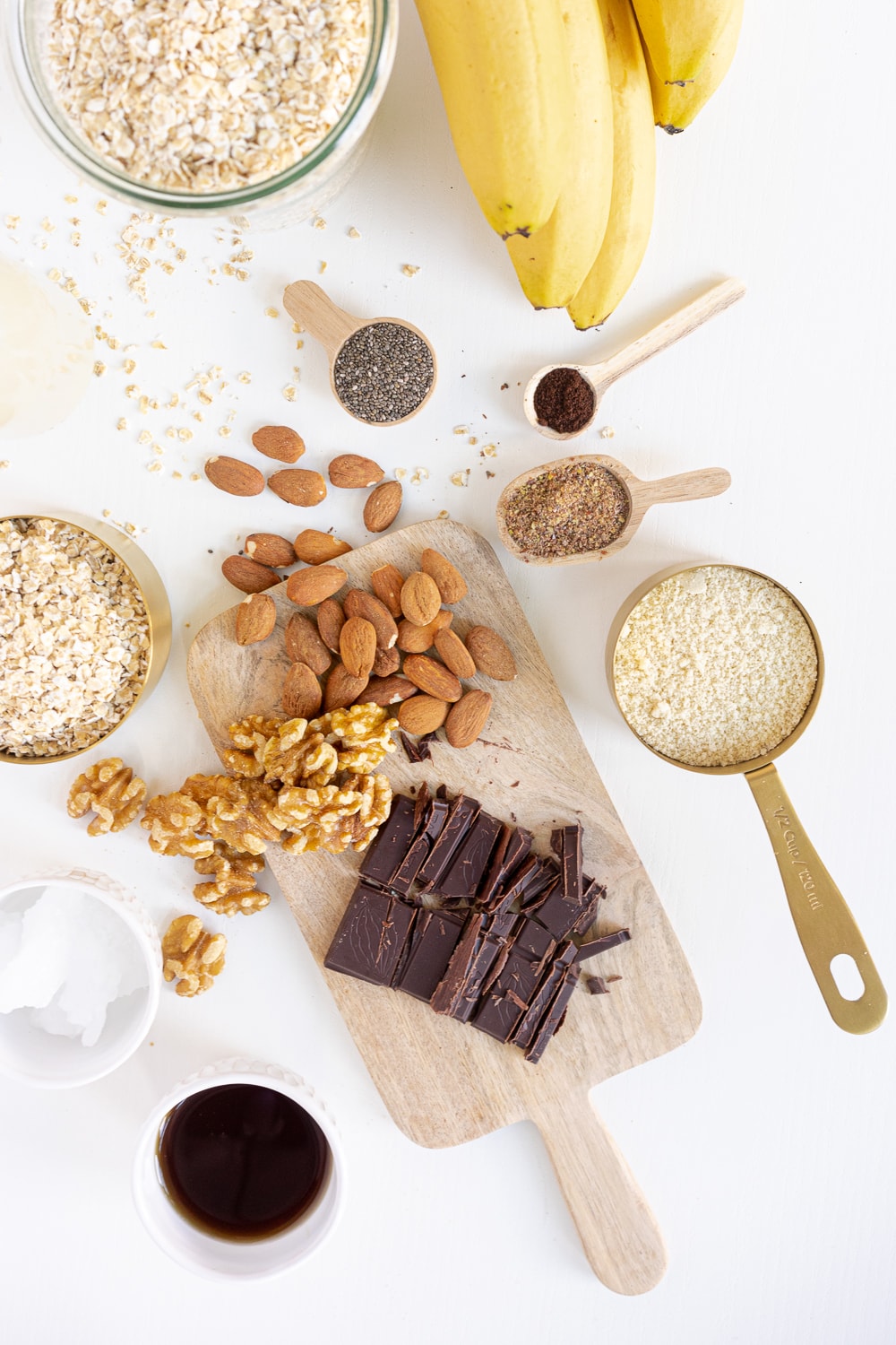 Top view of all ingredients needed to make my healthy breakfast cookies: rolled oats, bananas, almonds, walnuts, dark chocolate, flax seeds, chia seeds, maple syrup, coconut oil