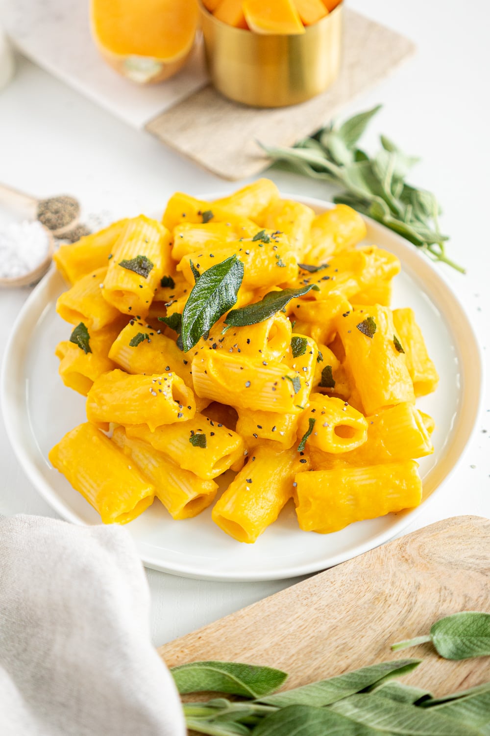 3/4 view of white plate filled with creamy butternut squash pasta topped with sage leaves