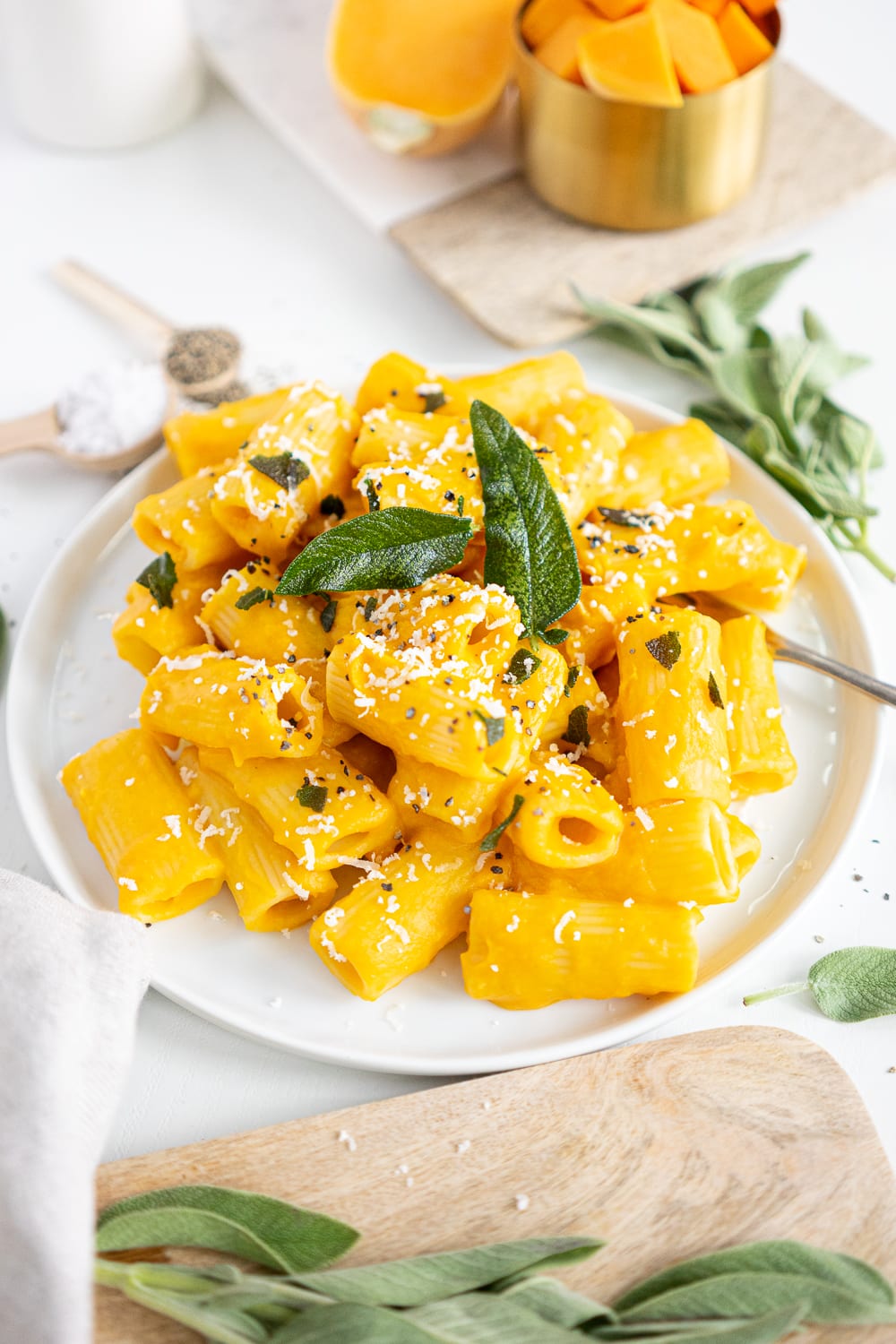 3/4 view of white plate filled with creamy butternut squash pasta topped with sage leaves