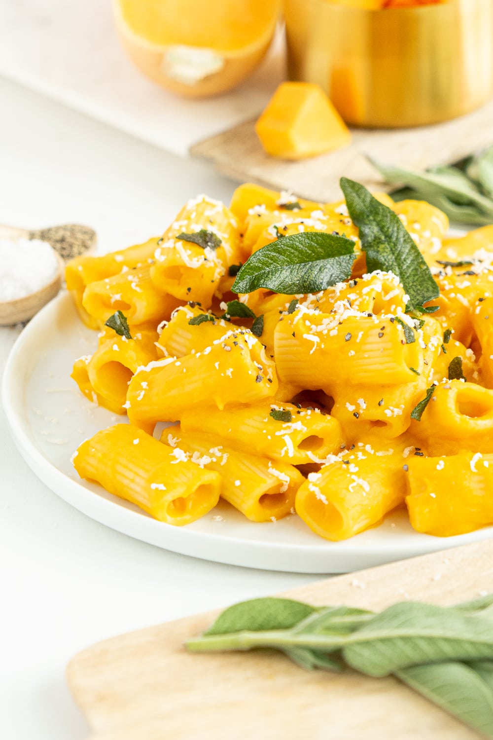 3/4 view of white plate filled with creamy butternut squash pasta topped with sage leaves