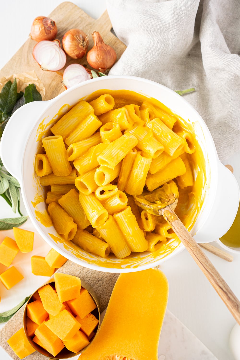 Top view of white pan with pasta and butternut squash sauce, being mixed with wooden spoon