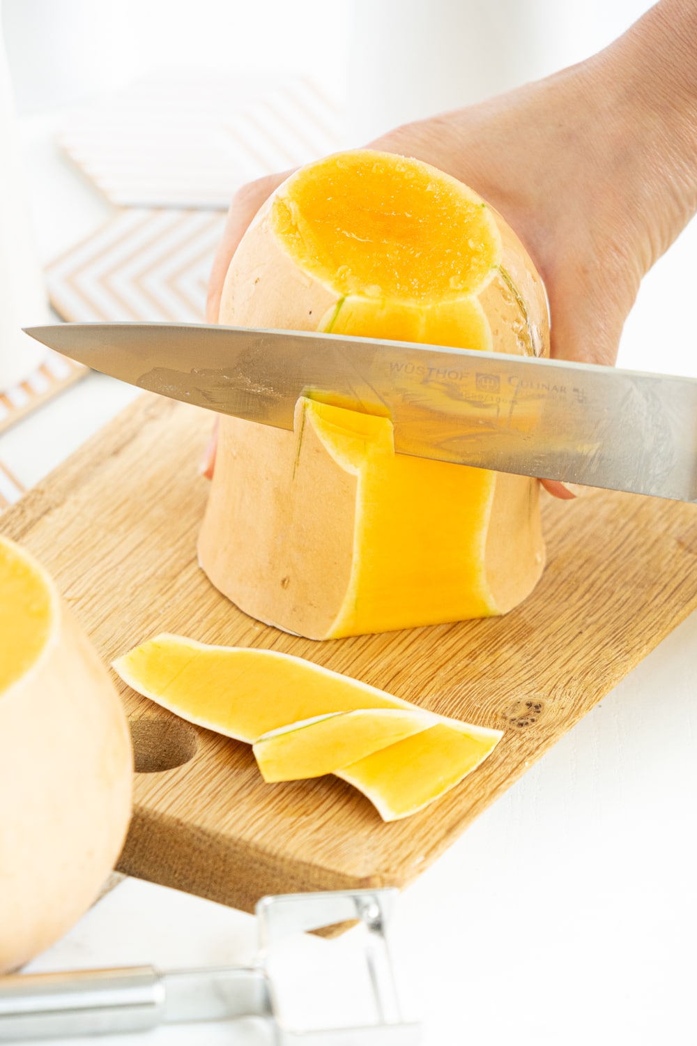 Hands peeling a butternut squash with a big knife