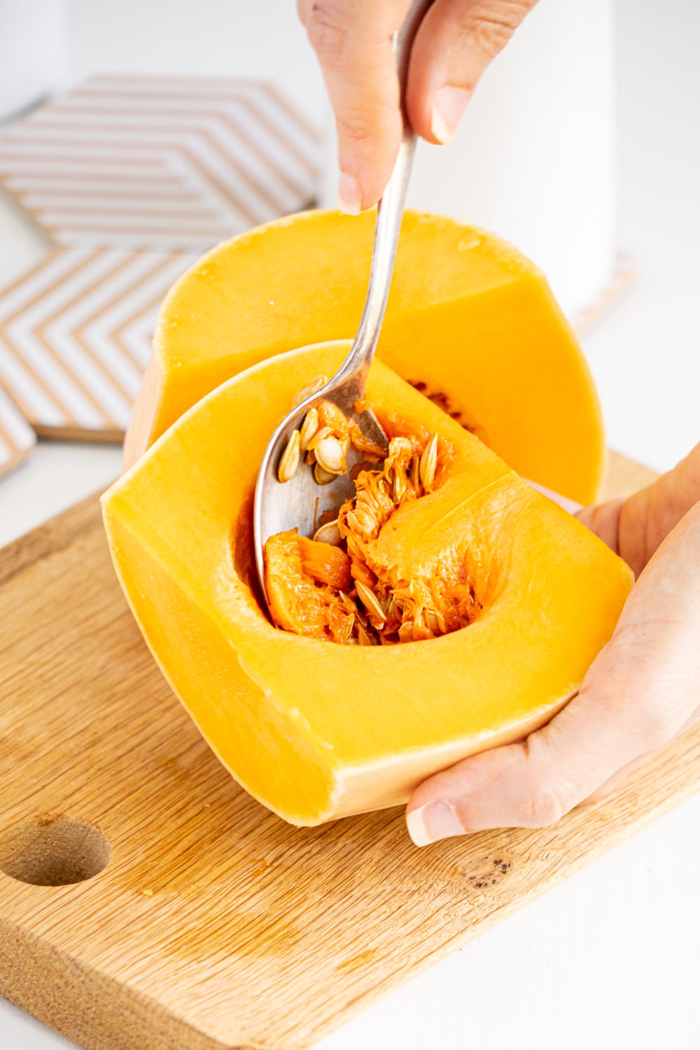 Hands removing seeds from butternut squash using a spoon