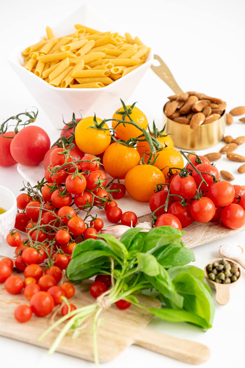 Top view of all ingredients needed to make a no-cook creamy tomato pasta: fresh tomatoes, fresh basil, garlic, extra-virgin olive oil, almonds, capers, salt, pasta