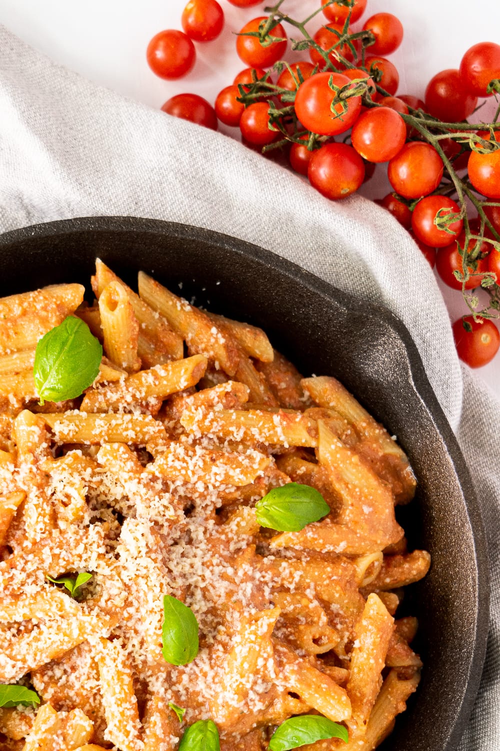 top view of iron skillet with creamy tomato pasta topped with basil leaves and vegan parmesan