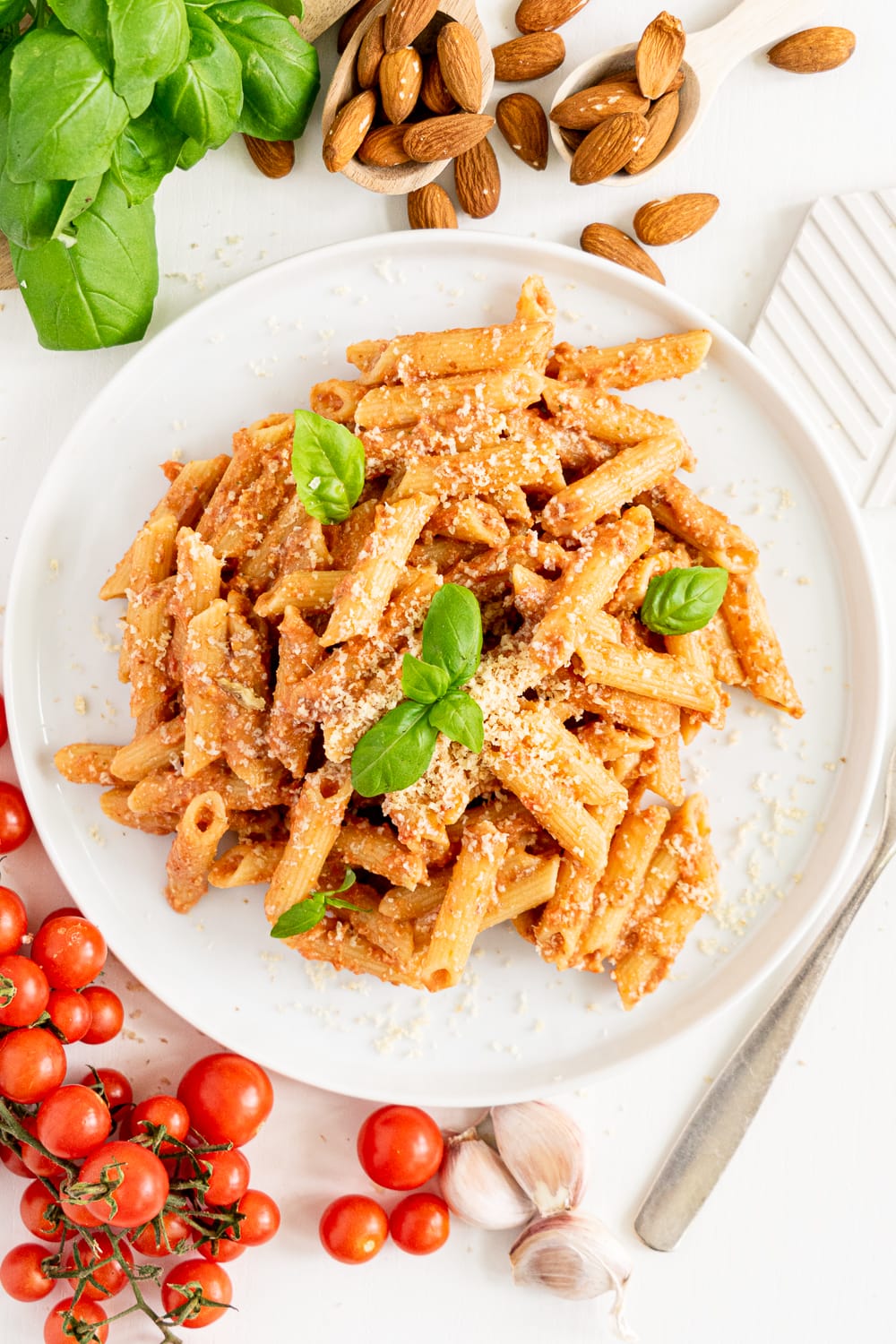 top view of white plate with creamy tomato pasta topped with basil leaves and vegan parmesan