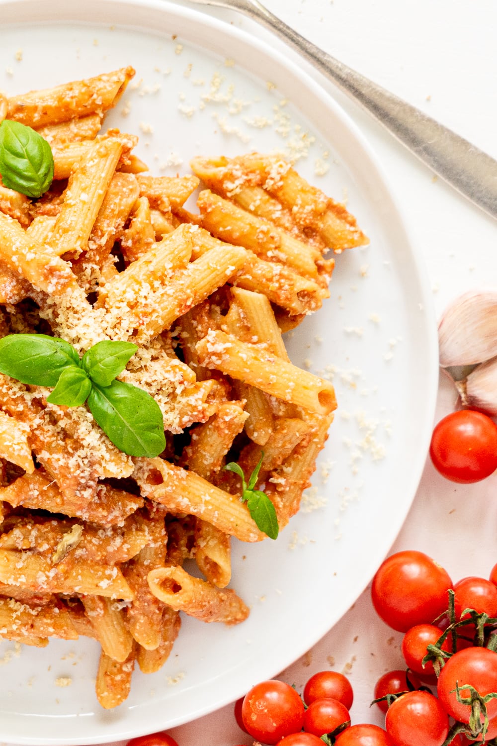 top view of white plate with creamy tomato pasta topped with basil leaves and vegan parmesan