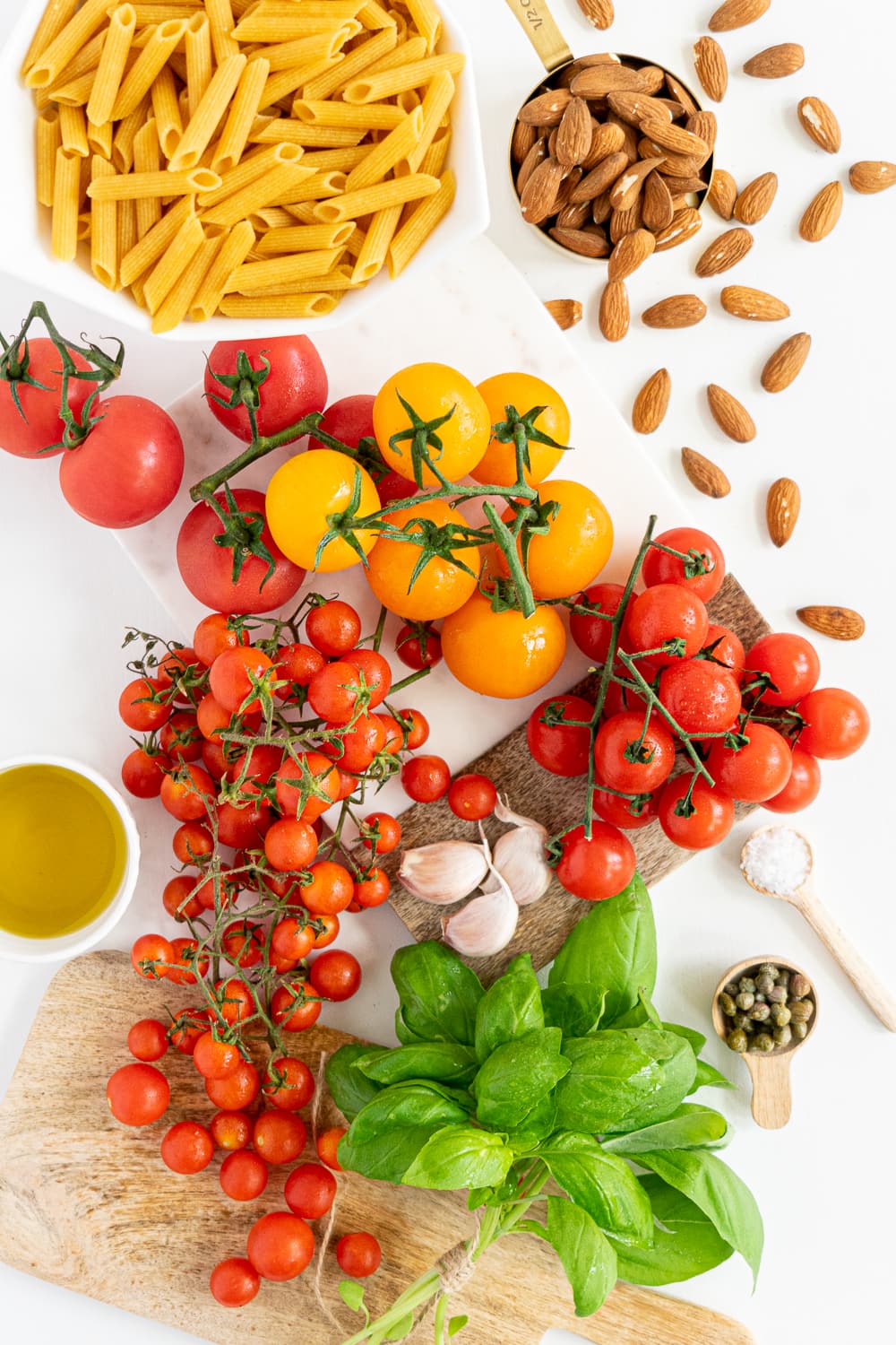 Top view of all ingredients needed to make a no-cook creamy tomato pasta: fresh tomatoes, fresh basil, garlic, extra-virgin olive oil, almonds, capers, salt, pasta
