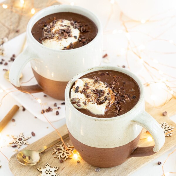 Three quarter view of healthy hot chocolate mugs with coconut whipped cream and cacao nibbles
