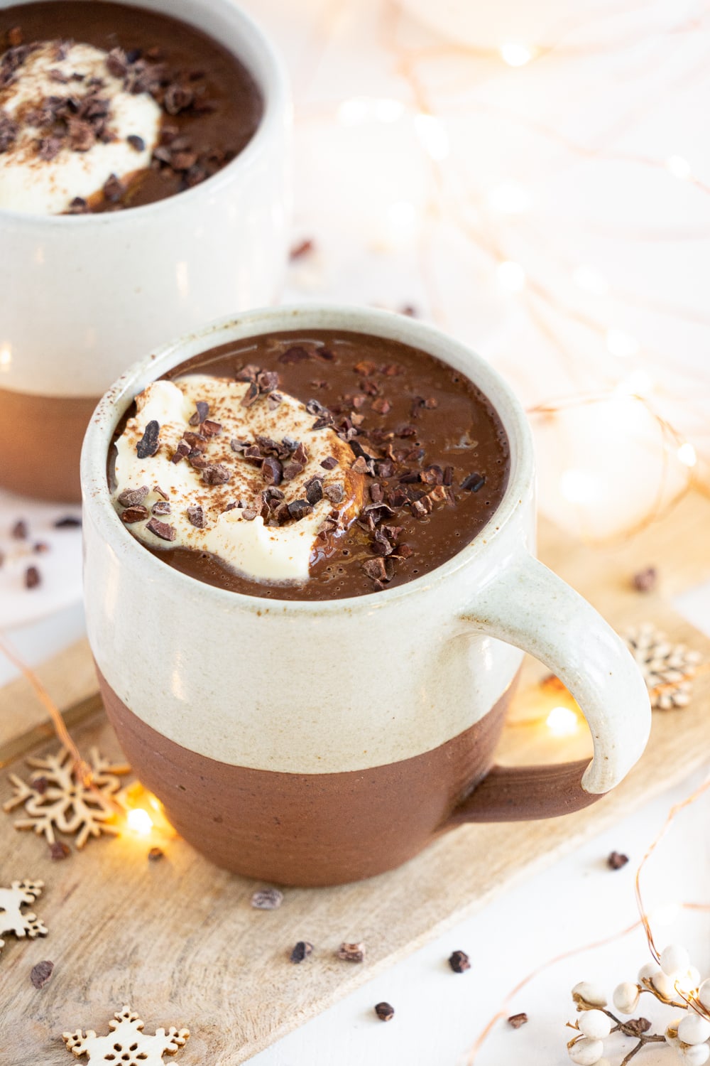 Three quarter view of healthy hot chocolate mugs with coconut whipped cream and cacao nibbles