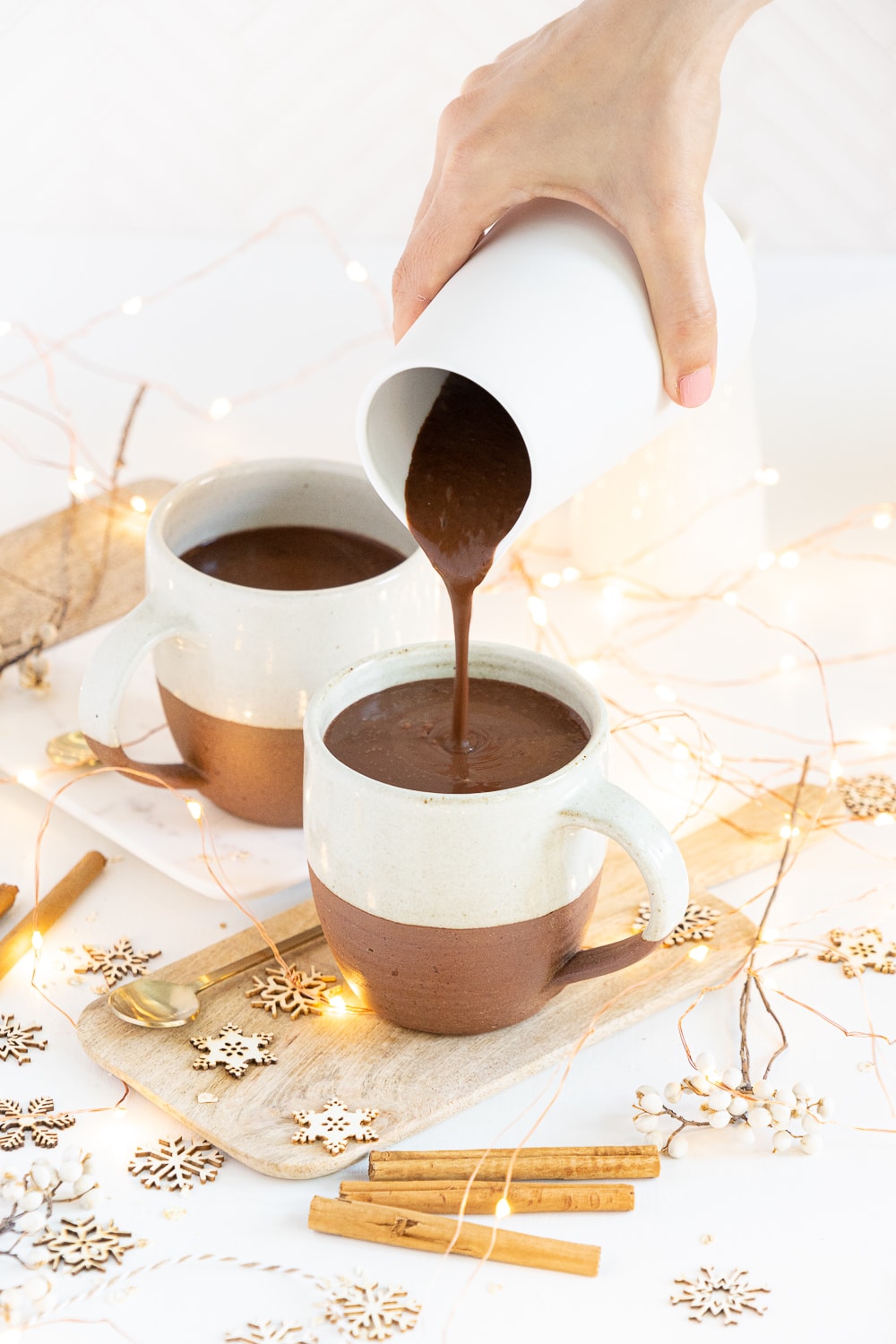 Hand pouring hot chocolate into a mug from a small white jug