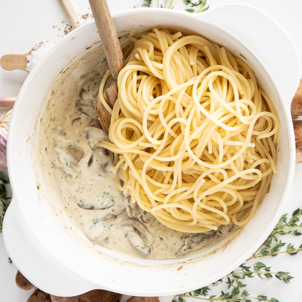 Top view of white pot with cooked mushrooms, cream and pasta ready to be tossed