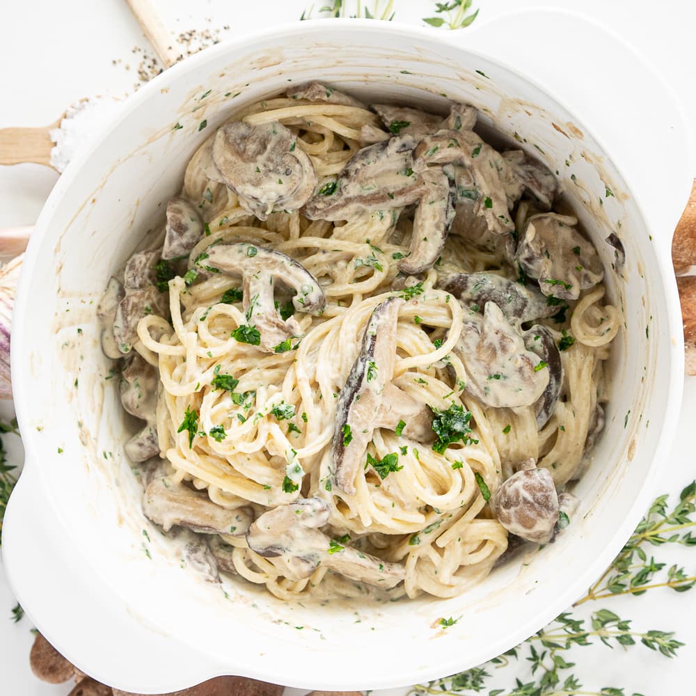 Top view of white pot with cooked mushrooms, cream and tossed pasta