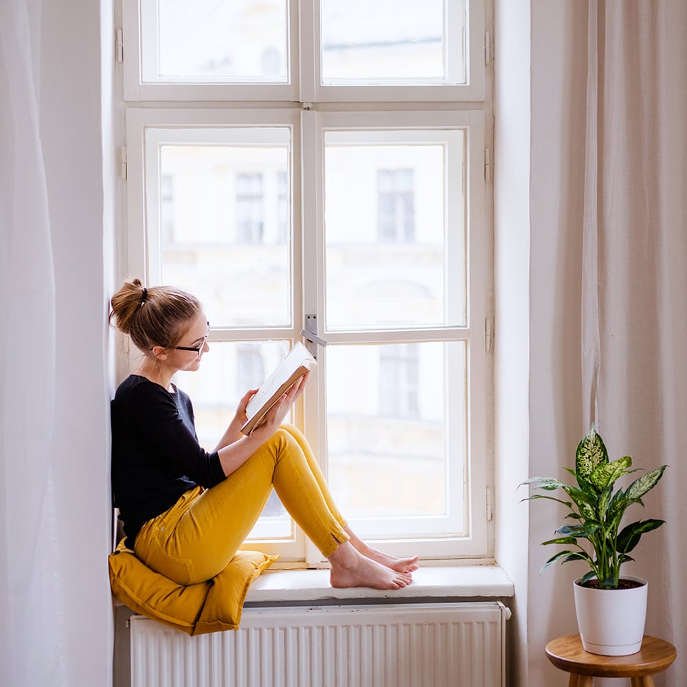 Mujer leyendo un libro en un rincón de la ventana