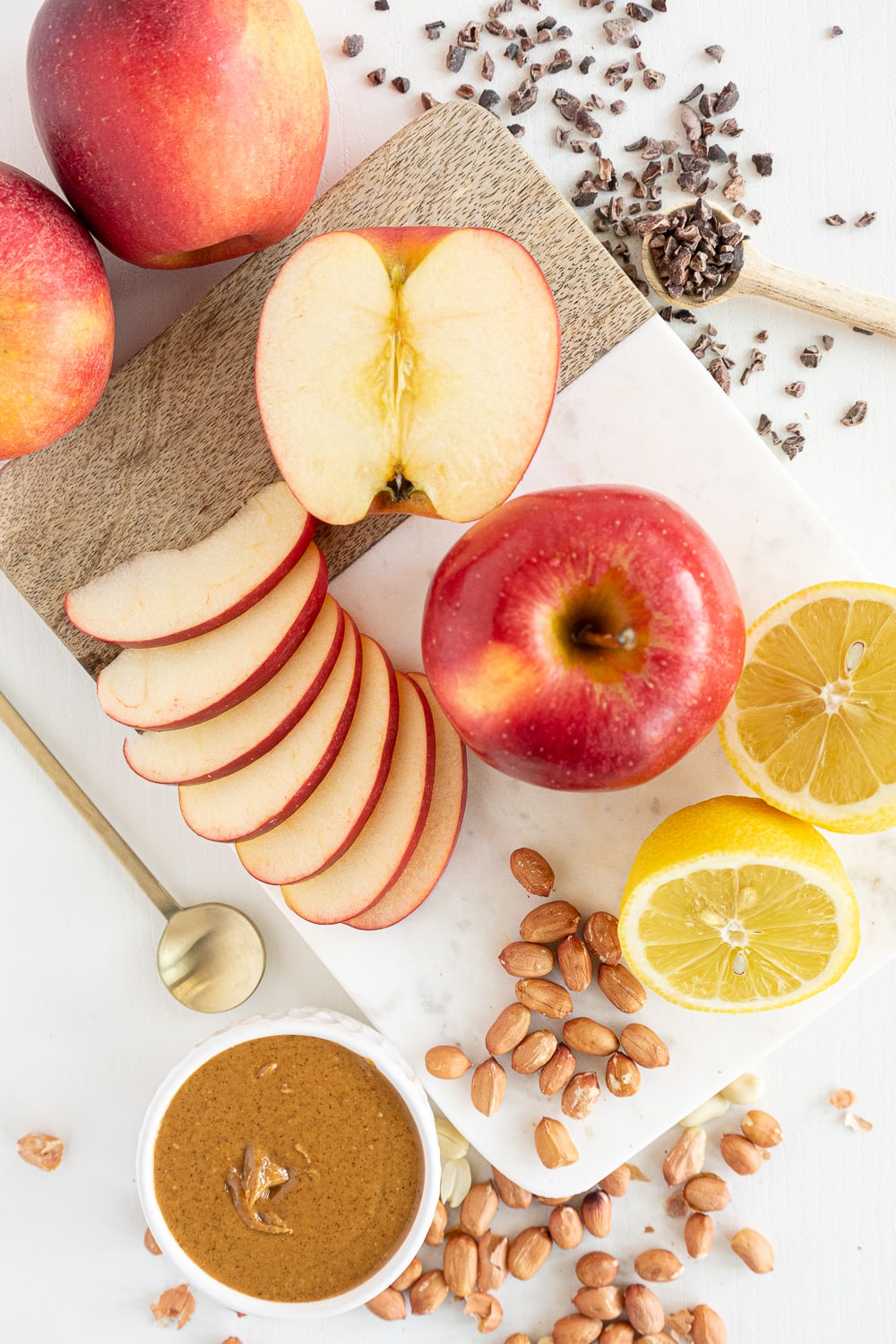 Top view of ingredients needed to make apple nachos: apples, peanut butter, chocolate nibs, lemon