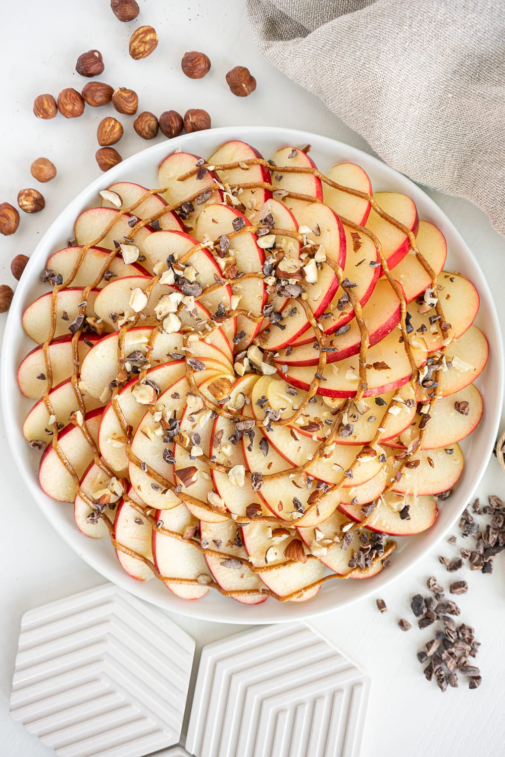 Top view of apple nachos with peanut butter, chocolate nibs, and chopped nuts