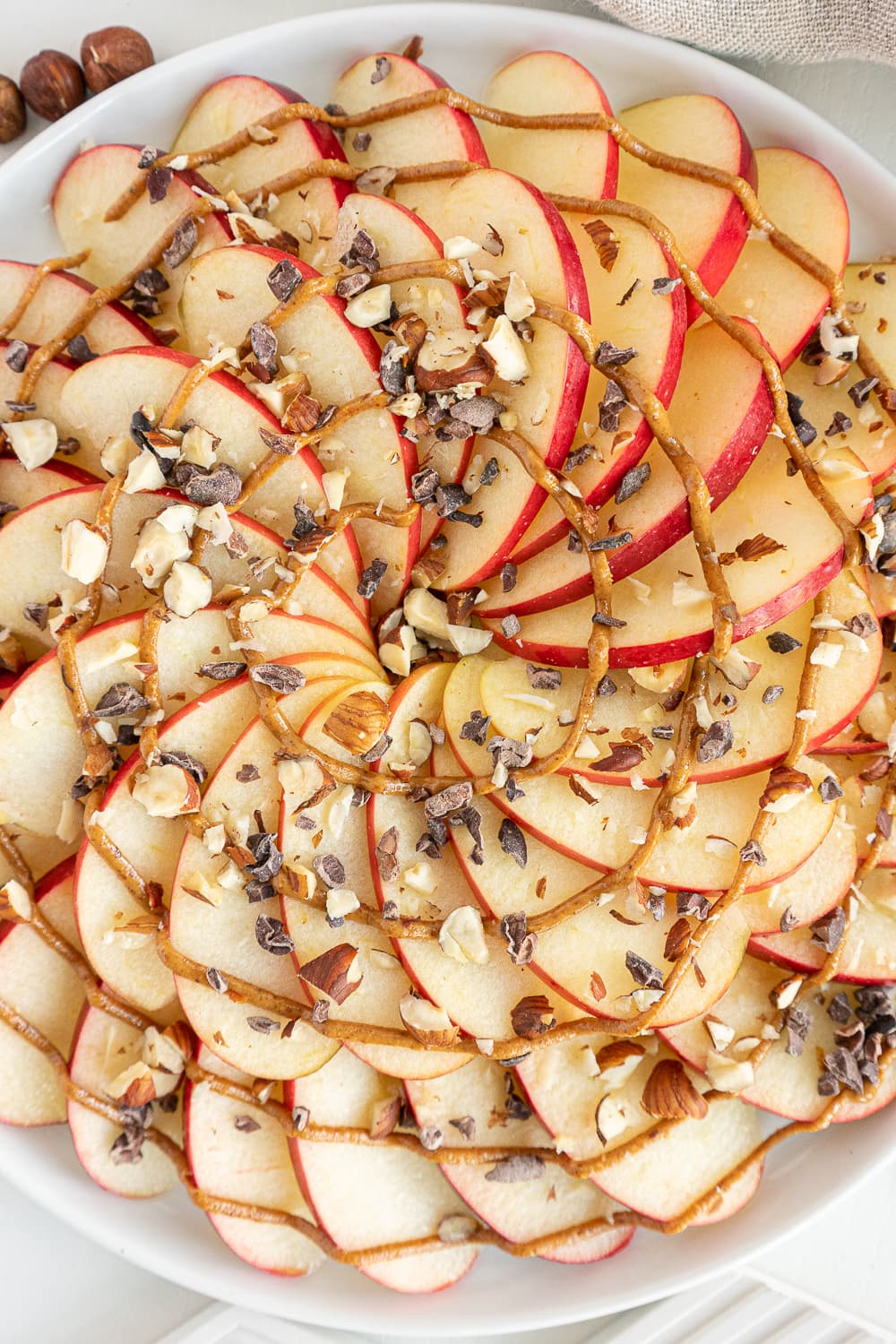 Top view of apple nachos with peanut butter, chocolate nibs, and chopped nuts