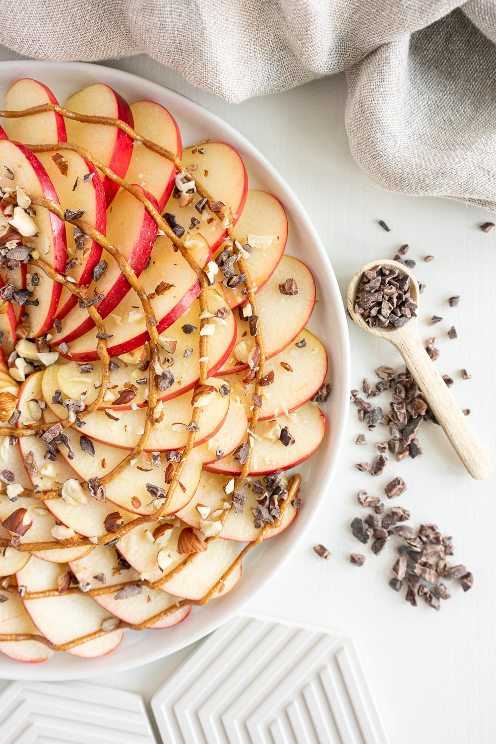 Top view of half a plate filled with apple nachos with peanut butter, chocolate nibs, and chopped nuts