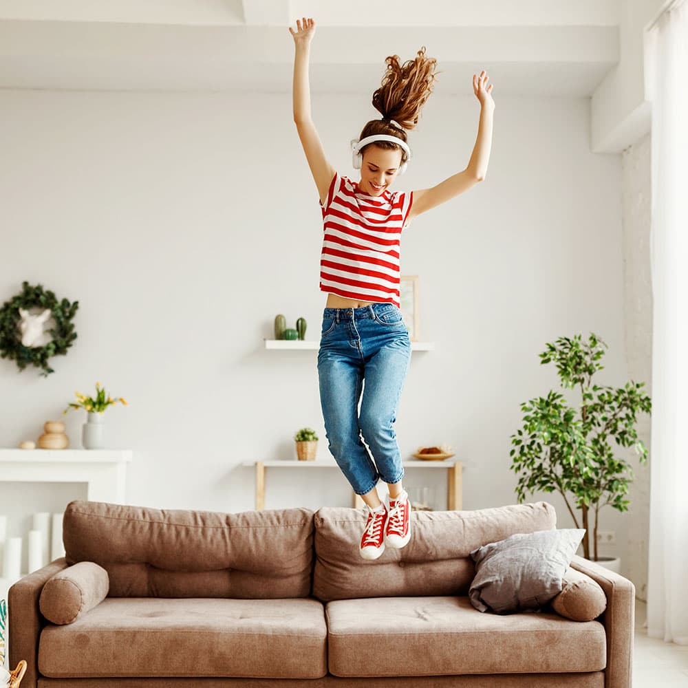 Mujer saltando en un sofá feliz de encontrar cómo ganar $1000 al mes