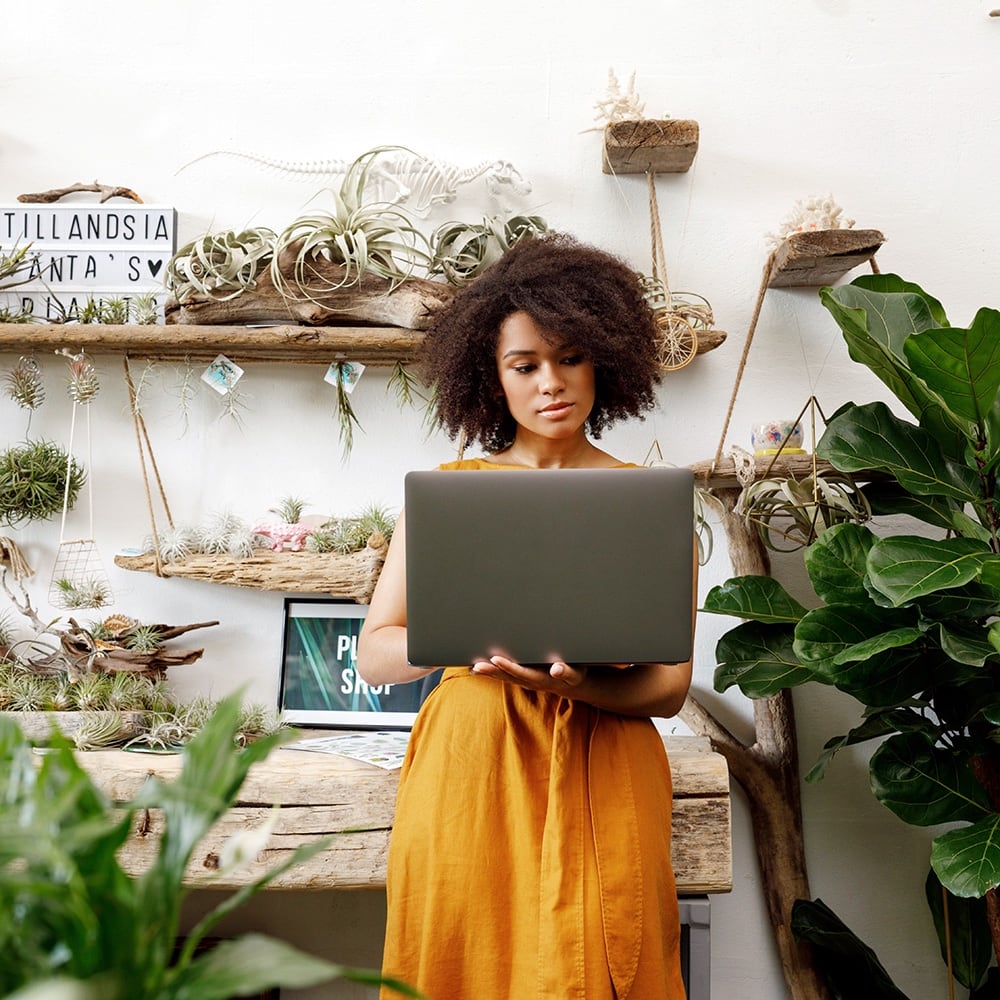 Mujer rodeada de plantas trabajando en su laptop