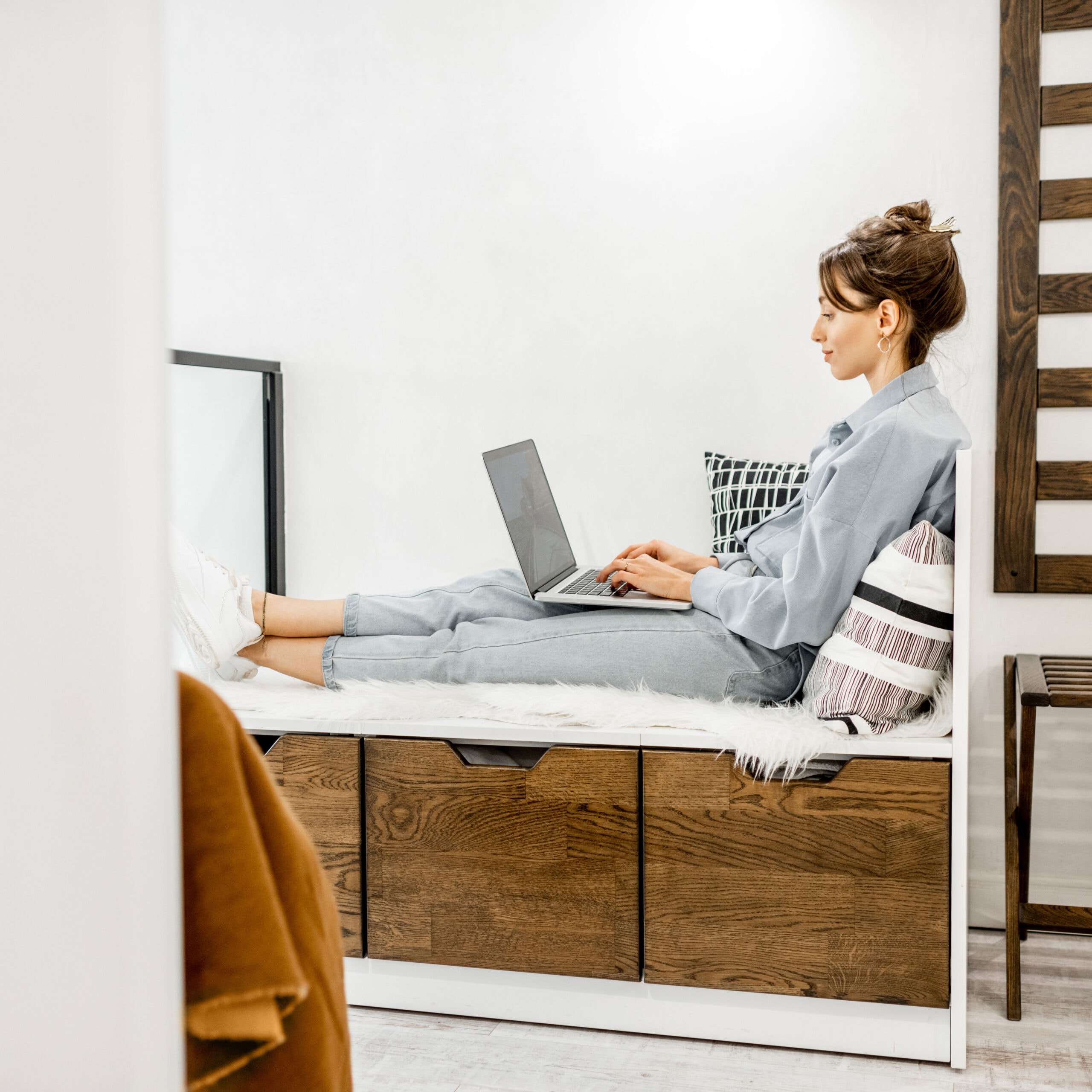 Asistente virtual escribiendo en una computadora portátil, sentada en un banco en su departamento