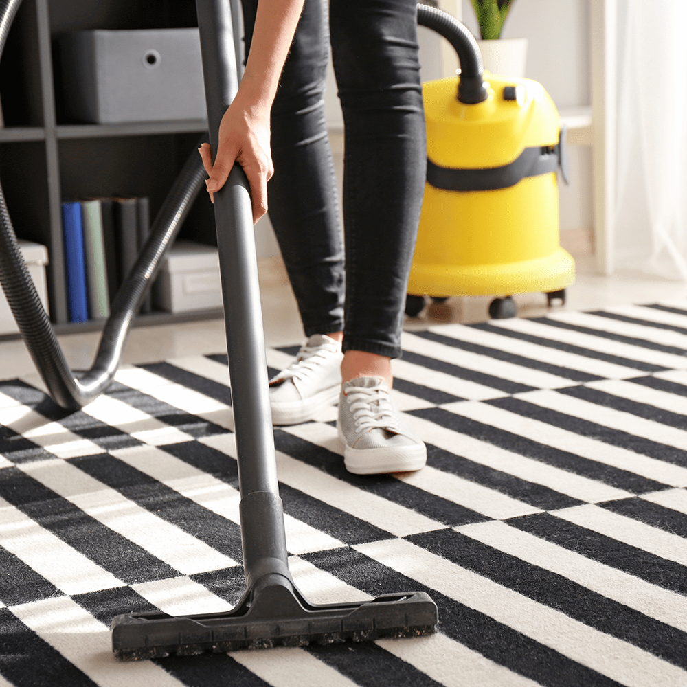 Woman cleaning rug with a hoover 