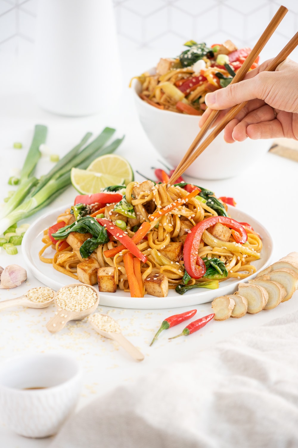 Hands with chopsticks picking up vegan stir-fried noodles from a white plate