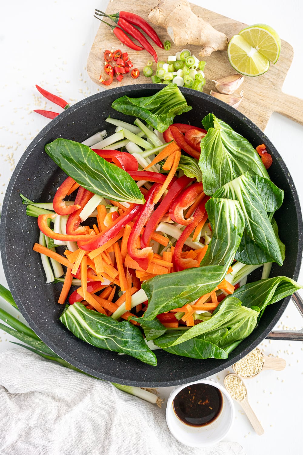 Vegetables (carrots, peppers, greens) stir-frying in a black pan