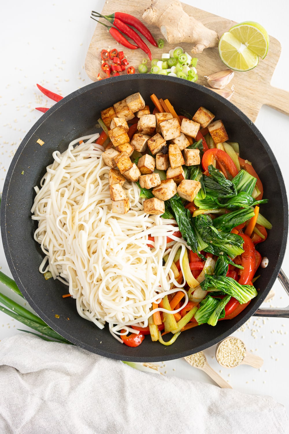 Top view of pan with noodles, greens, veggies and tofu, before mixing