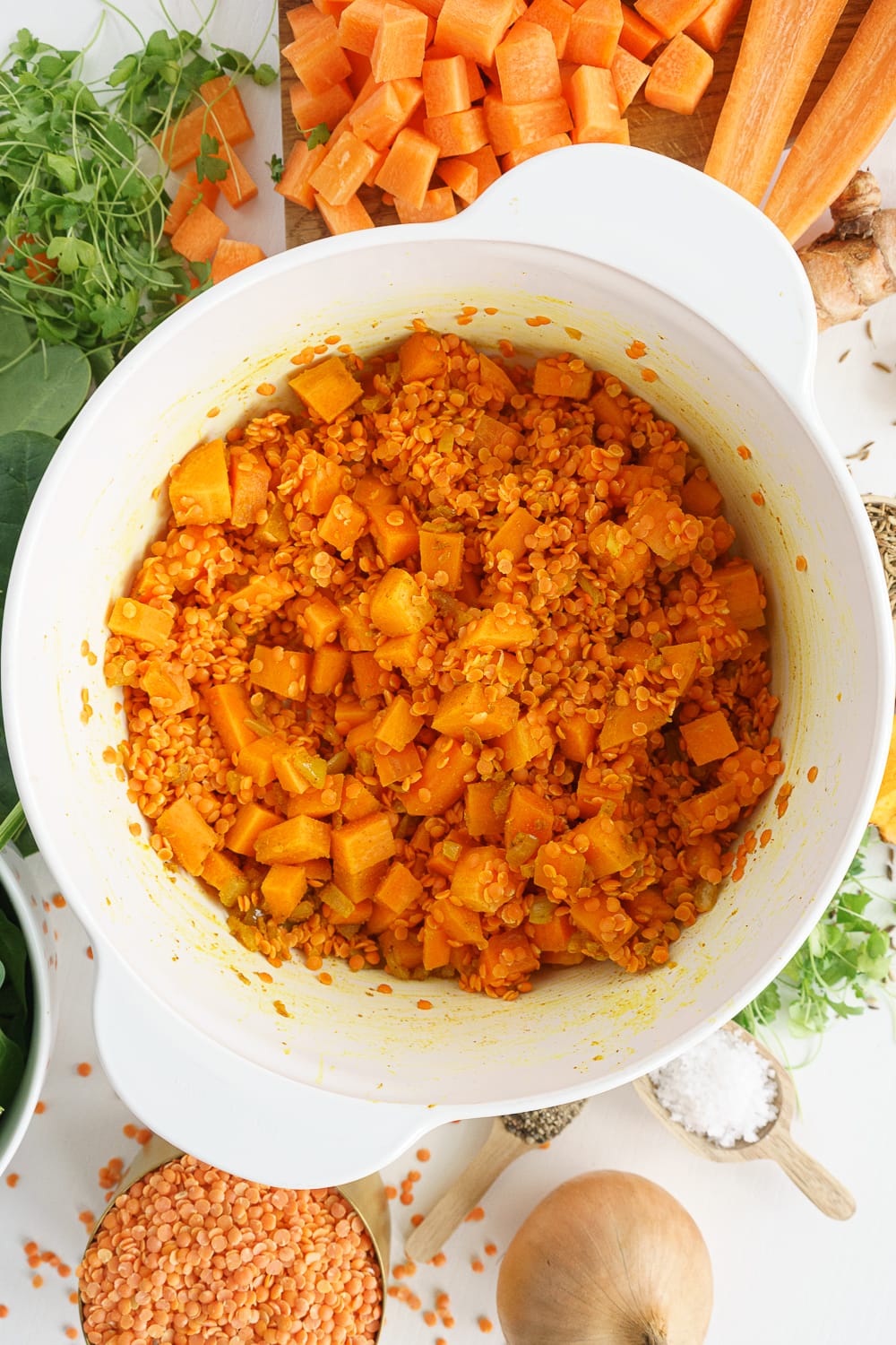 Overhead shot of white pot with carrots, spices, and red lentils