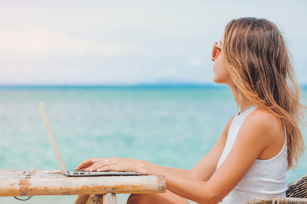 A photo of woman working on a laptop from a beach as an example of the top stock photos to sell online