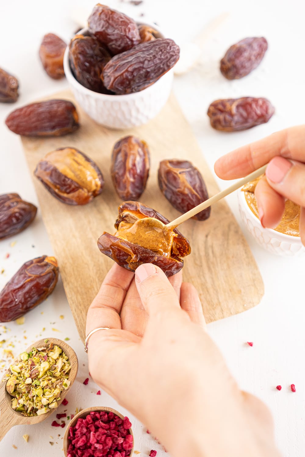 Hands filling a date with a teaspoon of peanut butter