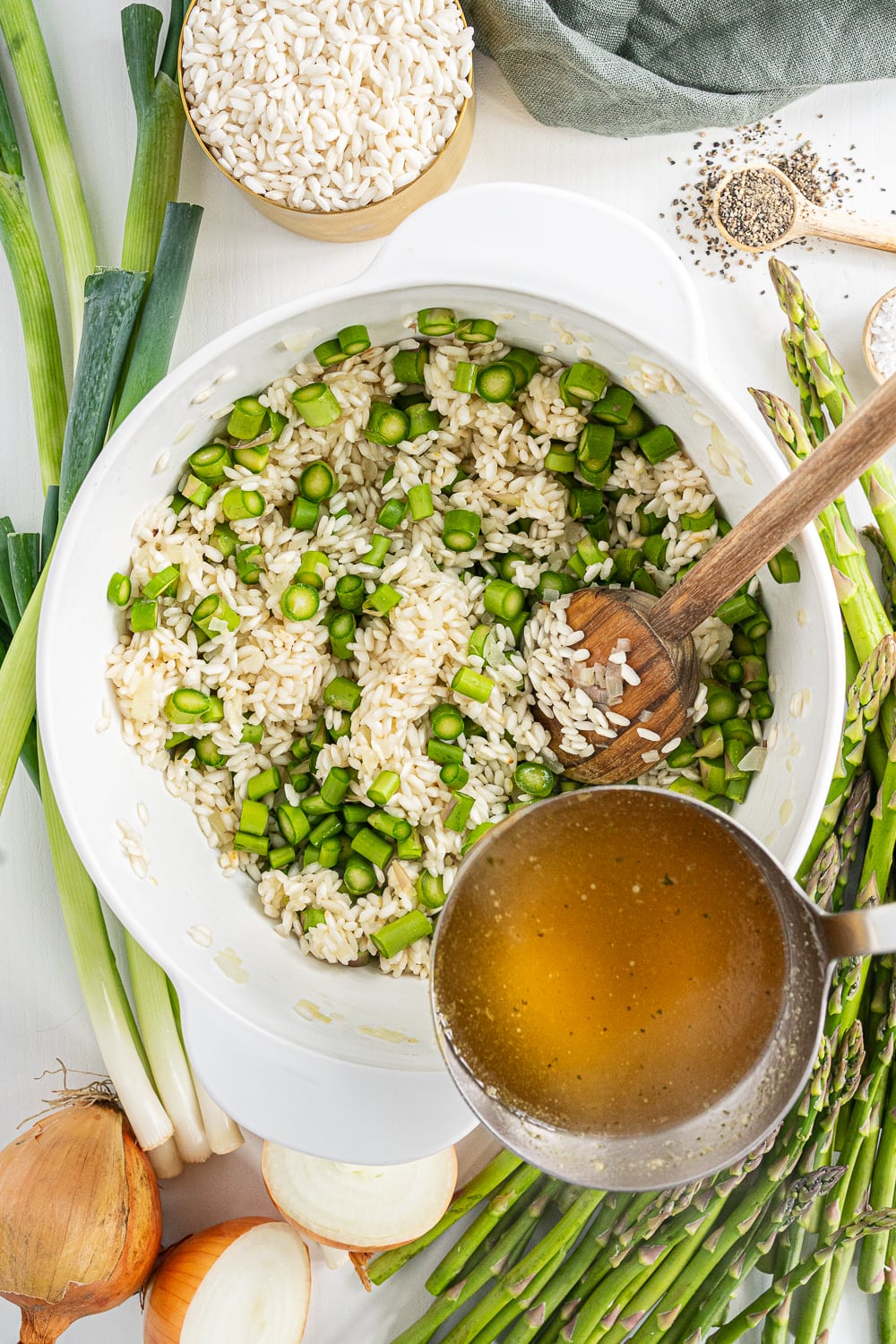 Broth being poured into pot with rice and asparagus