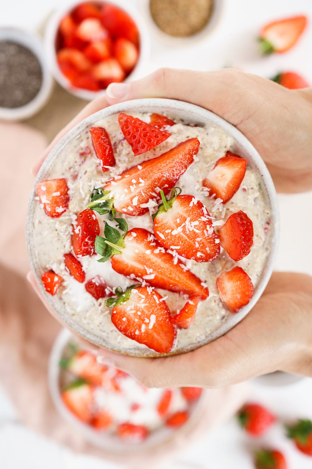 Hands holding a bowl filled with strawberry overnight oats