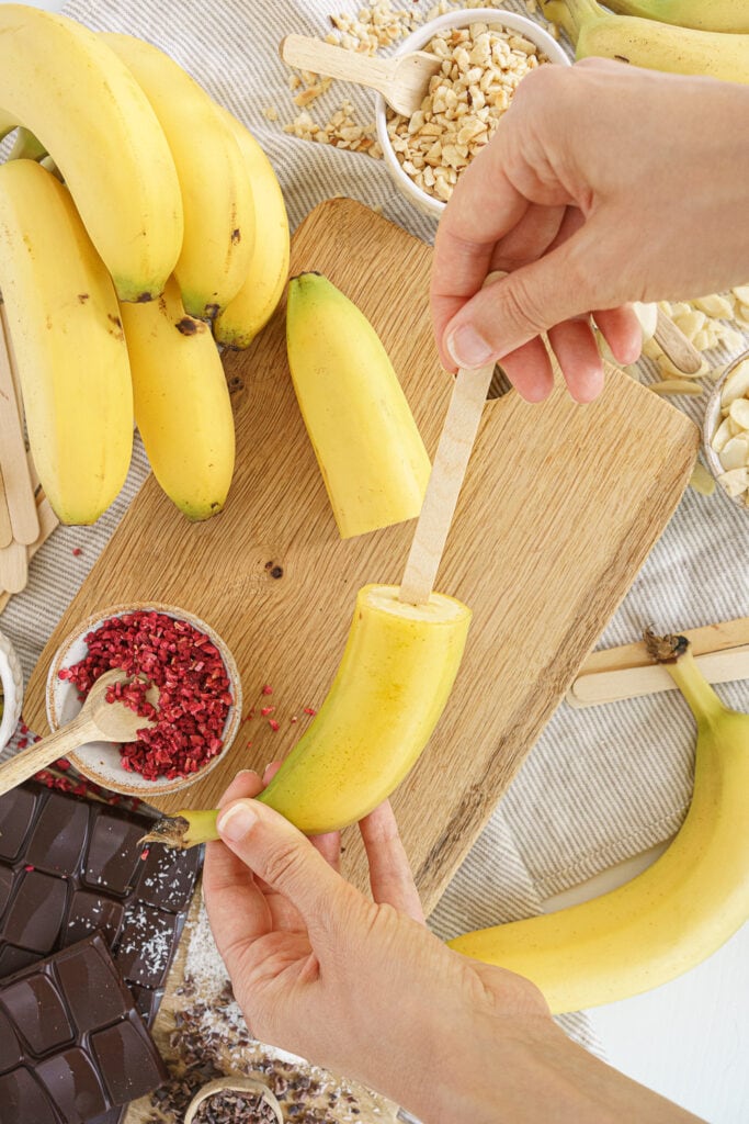 hands inserting a popsicle stick into a banana