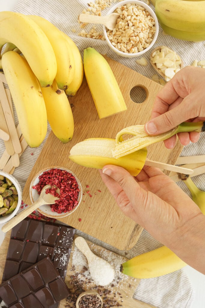 hands peeling half a banana if a popsicle stick in it