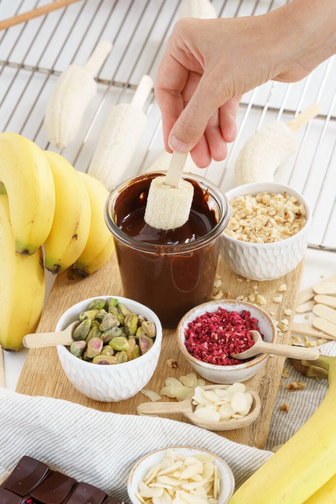 hand dipping a banana on a stick in melted chocolate